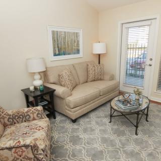 A cozy living room with a sofa, armchair, lamps, and a coffee table, featuring neutral tones and a geometric rug.