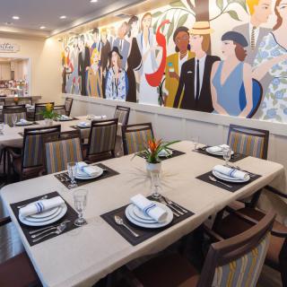 A beautifully decorated restaurant interior featuring a colorful mural on the wall and neatly arranged dining tables with elegant place settings.