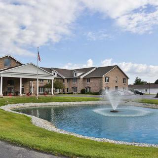 A scenic view of a building with a fountain in a pond under a partly cloudy sky.