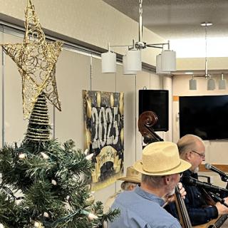 A festive indoor scene featuring a decorated Christmas tree and musicians performing, celebrating the holiday spirit.
