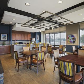 Modern dining area with kitchen, featuring tables, chairs, and large windows.