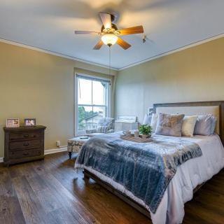 A cozy bedroom with a large bed, wooden flooring, and a ceiling fan.