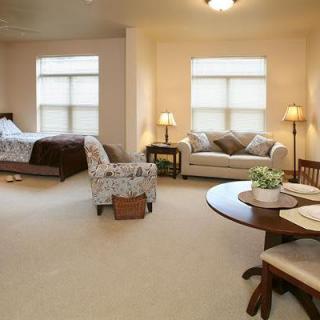 A cozy living space with a bedroom area, featuring a sofa, chairs, and a dining table.
