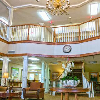 A spacious and elegantly decorated lobby with a chandelier, comfortable seating, a central staircase, and indoor plants.