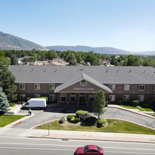 A sunny day view of a hotel surrounded by lush trees and mountains in the background.