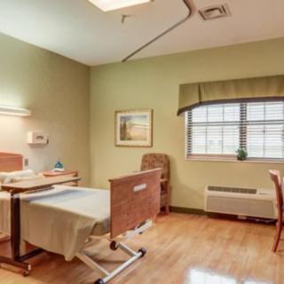 A well-lit hospital room featuring a bed, chair, and window.