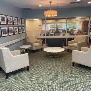 A cozy waiting room featuring armchairs and a round coffee table with framed pictures on the wall.