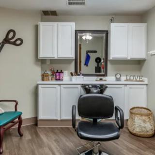 A hair salon interior featuring a styling chair in front of a mirror and cabinets, with decorative scissors on the wall.