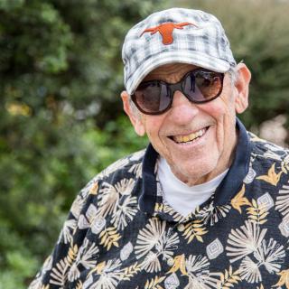 A smiling elderly man wearing sunglasses and a hat, enjoying time outdoors.