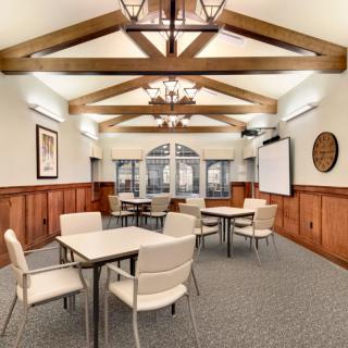 A stylish conference room with wooden beams and chandeliers, featuring tables and chairs arranged for a meeting.