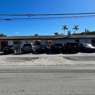 A sunny day shows a parking lot filled with cars in front of a building surrounded by palm trees.