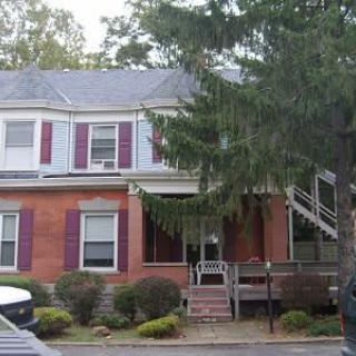 A two-story brick house with a porch and surrounding trees.