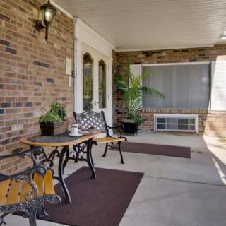 A cozy porch with a brick wall, featuring a table and chairs set up for outdoor seating, surrounded by potted plants.