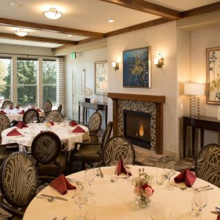 An elegant dining room with round tables set for a meal, featuring a cozy fireplace and tasteful artwork on the walls.