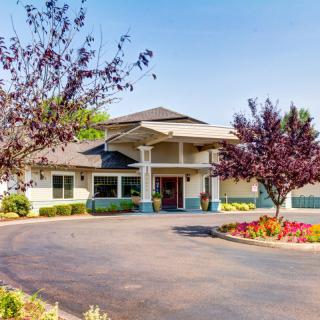 A well-maintained building surrounded by trees and flowers, with a circular driveway leading to the entrance.