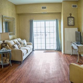 A cozy living room with a sofa, wooden flooring, and ample natural light streaming through large windows.