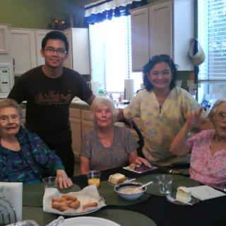 A group of people gathering around a table in the kitchen, enjoying a meal together.