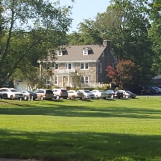 A scenic view of a large house surrounded by vehicles parked on a green lawn.