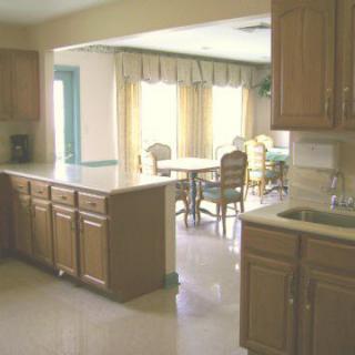 A kitchen interior with wooden cabinets and a dining area in the background.