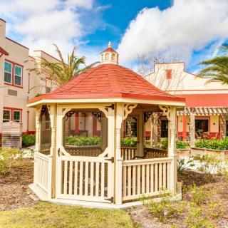 A charming gazebo situated in a landscaped garden on a sunny day, with buildings in the background.