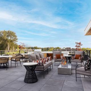 A spacious outdoor patio with comfortable seating and tables, surrounded by nature under a clear blue sky.