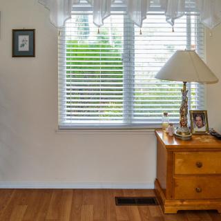 A cozy bedroom corner with a wooden nightstand, lamp, and window with blinds.