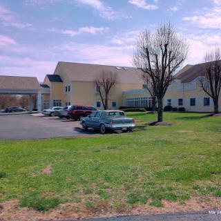 A view of a building complex with trees and parked cars on a grassy area under a cloudy sky.