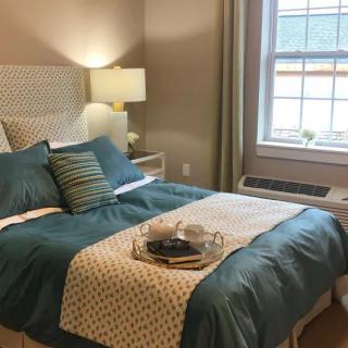 A cozy bedroom with a neatly made bed, decorative pillows, and a warm lamp by the window.