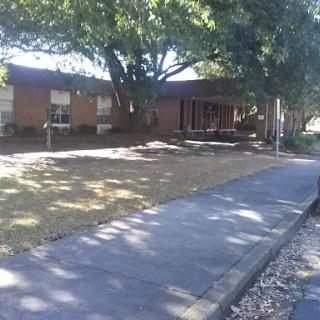 A peaceful outdoor view featuring a building surrounded by trees and a pathway.