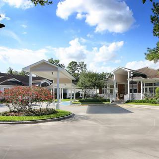 A sunny day view of a large building with a driveway and landscaped surroundings.
