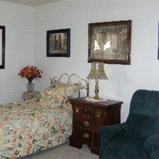 A cozy bedroom featuring a floral-patterned bed, a side table with a lamp, and an armchair.