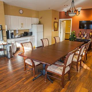 A well-furnished dining area with a large table, kitchenette, and a television.