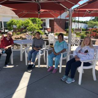 A group of people sitting outdoors under red umbrellas enjoying a sunny day.