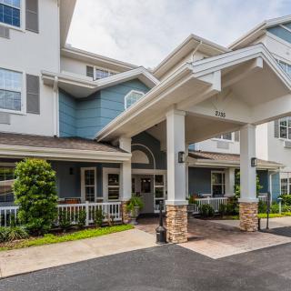 The image shows the entrance of a residential building with a porch and landscaped surroundings.