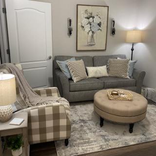 A cozy living room with a gray sofa, plaid armchair, and a round beige coffee table.