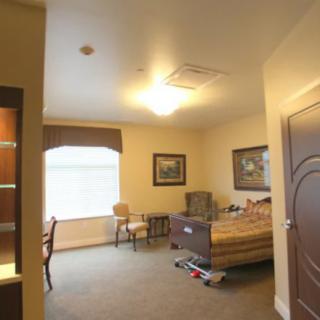 A well-lit room with a bed, chair, and window featuring decorative artwork.