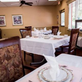 A well-set dining area with tables covered in white tablecloths, complete with plates and folded napkins, ready for guests.