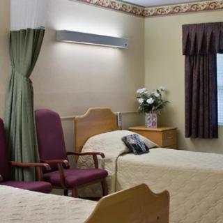 A hospital room with two beds, chairs, and a decorative vase of flowers.