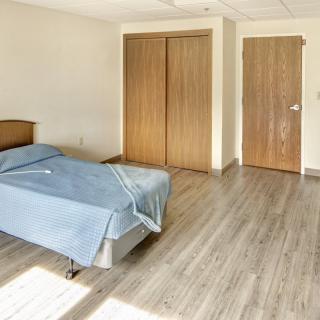 A minimalist bedroom with a single bed, wooden flooring, and a built-in closet.