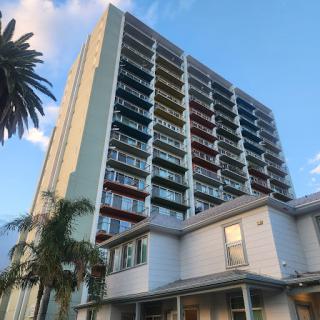 A modern high-rise building featuring multiple balconies and palm trees in the foreground.