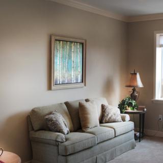 A cozy living room with a comfortable sofa, artwork on the wall, and a lamp by the window.
