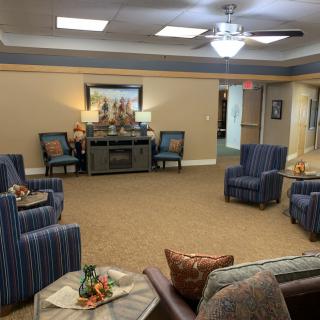 A cozy living room with chairs and a sofa arranged around a central table, featuring warm lighting and decorative elements.