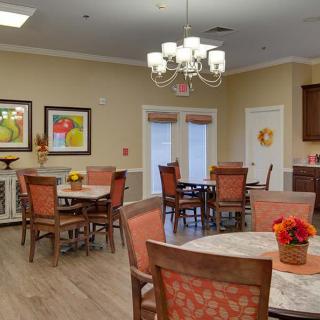 A cozy dining room with several tables and chairs, decorated with floral arrangements and paintings on the walls.