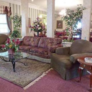 A cozy living room with a patterned sofa, armchair, and a glass coffee table adorned with floral arrangements.