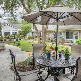 A cozy outdoor patio area with a table, chairs, and an umbrella, surrounded by a well-maintained garden.