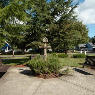 A peaceful park scene featuring benches, lush trees, and a birdhouse along a paved pathway.