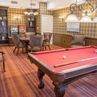 A cozy billiards room with a red felt pool table, elegant seating area, and warm lighting.