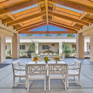 A sunny courtyard featuring a wooden-ceiling patio with a dining table and chairs.