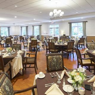 A spacious and elegantly set dining room with multiple tables and chairs, adorned with chandeliers.