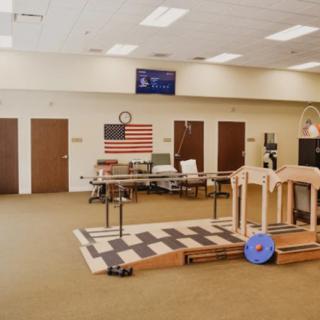 Interior of a physical therapy facility with various exercise equipment and an American flag on the wall.